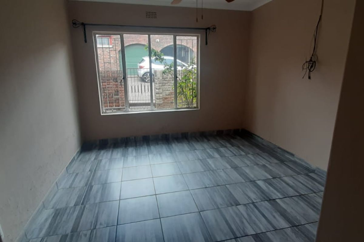 An empty bedroom featuring grey tiled flooring, a large window with security bars, and exposed electrical wiring on the wall.