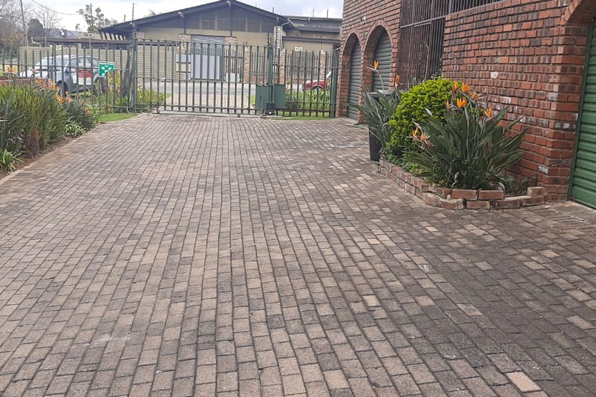 A paved driveway leading to a garage with brick facade and secure metal gate access.