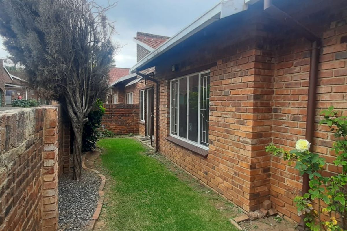 A view of the exterior rear of the townhouse, featuring face-brick walls, metal window security bars, and a small private garden area.