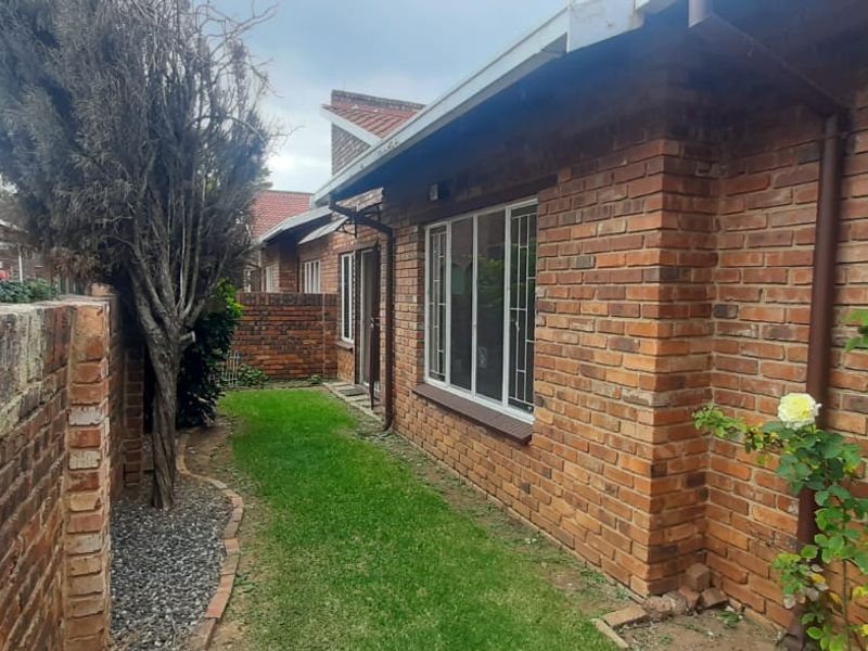 A view of the exterior rear of the townhouse, featuring face-brick walls, metal window security bars, and a small private garden area.