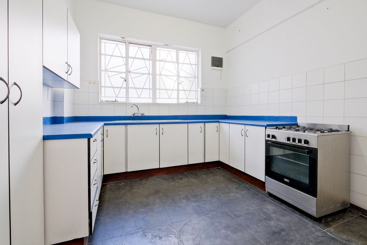 A functional kitchen featuring white cabinetry, blue countertops, tiled splashbacks, and a freestanding stove, offering a clean and practical workspace.