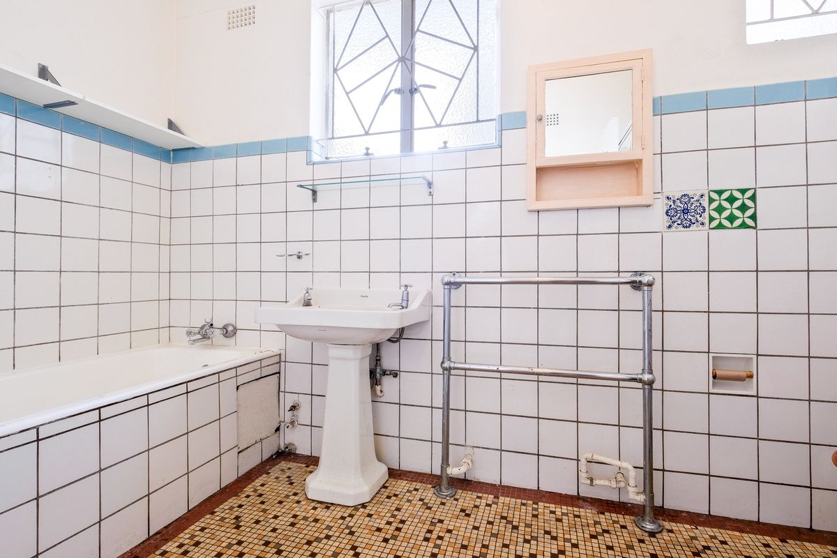 A dated bathroom featuring a pedestal basin, bathtub, and tiled walls with a mosaic floor finish, requiring modernization.