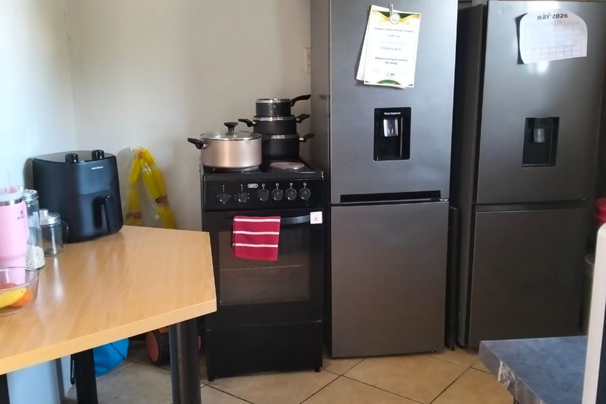 A functional kitchen area featuring tiled flooring, a freestanding stove, and space for multiple refrigeration units.