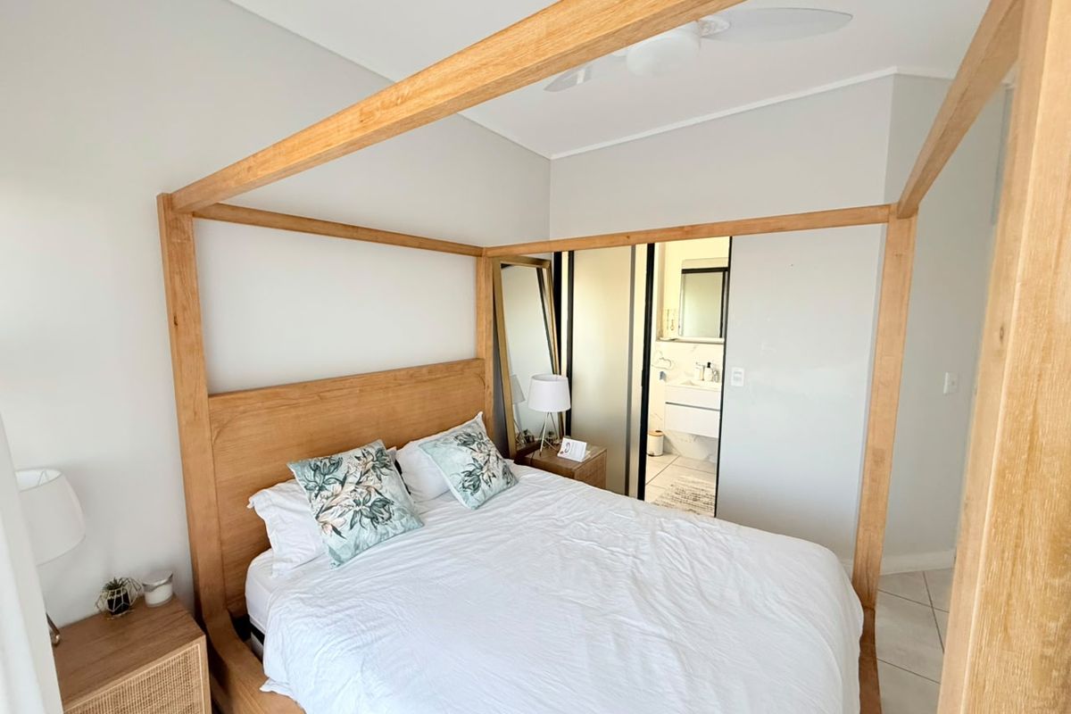 A well-maintained bedroom featuring neutral tones, tiled flooring, and an en-suite bathroom accessible through sliding doors.