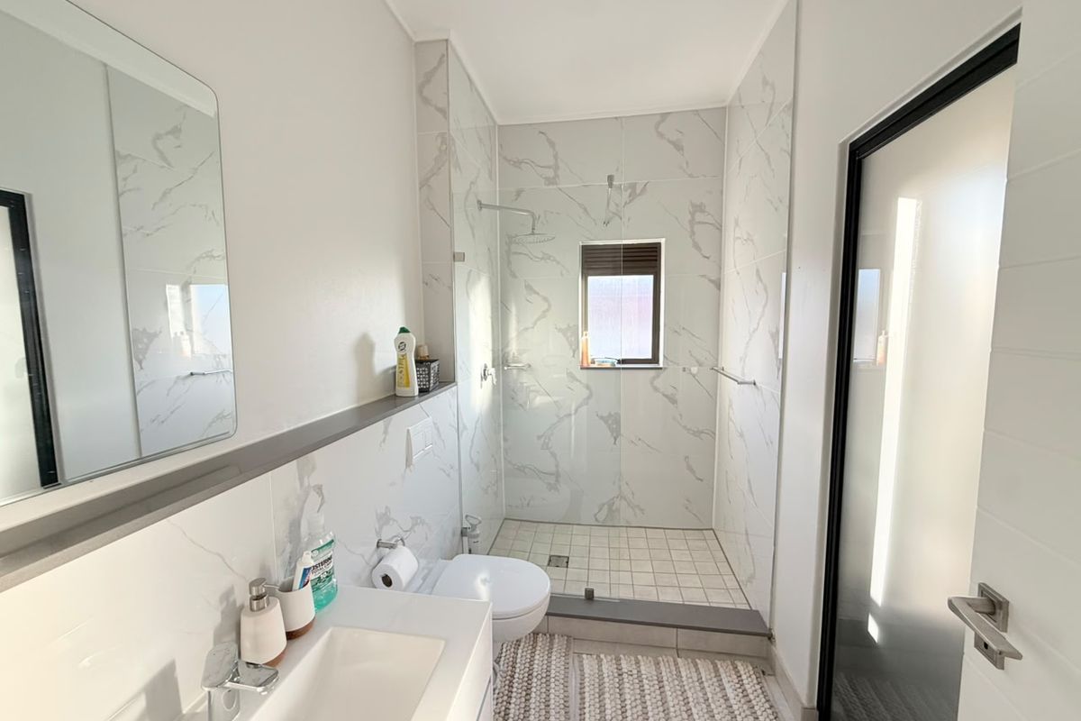 Modern bathroom featuring a walk-in shower with glass enclosure, marble-look wall tiles, wall-mounted toilet, and a sleek vanity with integrated basin.