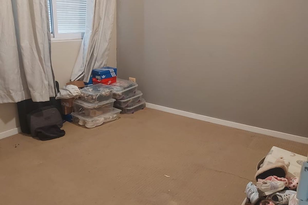 A bedroom featuring neutral wall paint, carpeted flooring, and a window with curtains, currently used for storage.