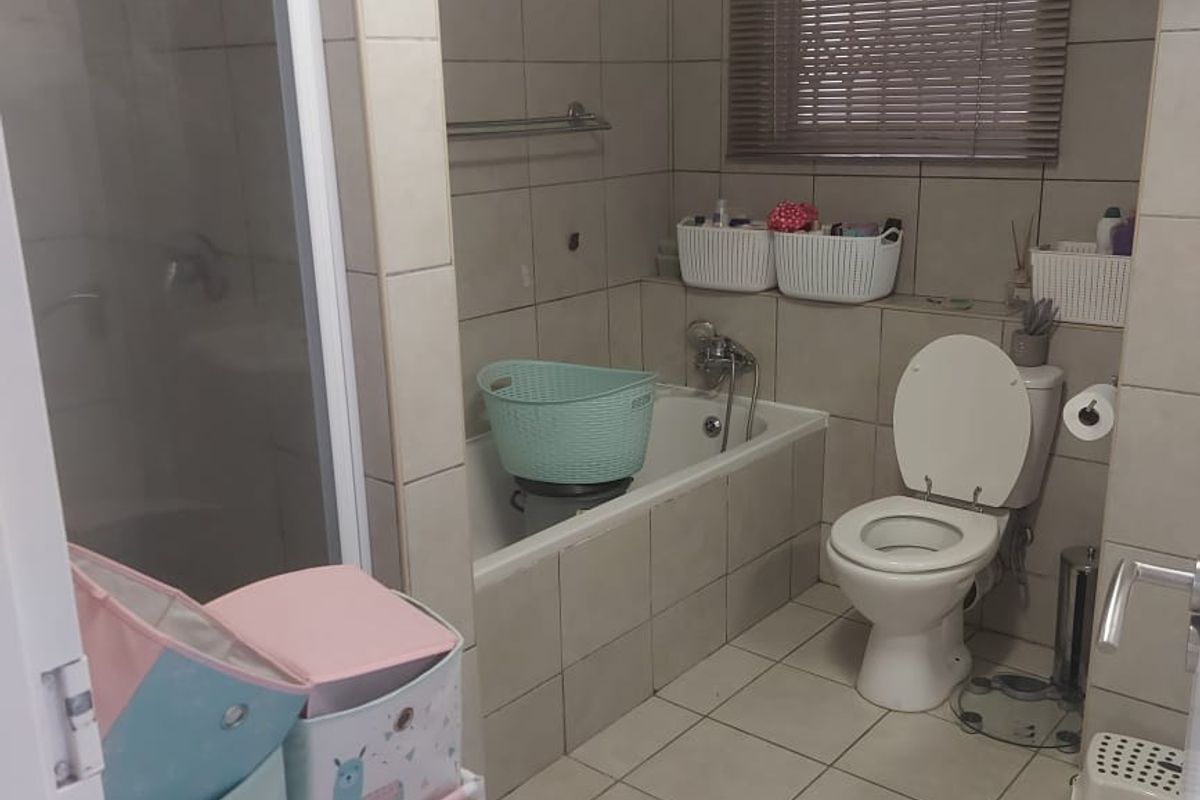 A functional bathroom featuring a tiled bathtub, separate glass-enclosed shower, and standard toilet with neutral wall and floor tiling.