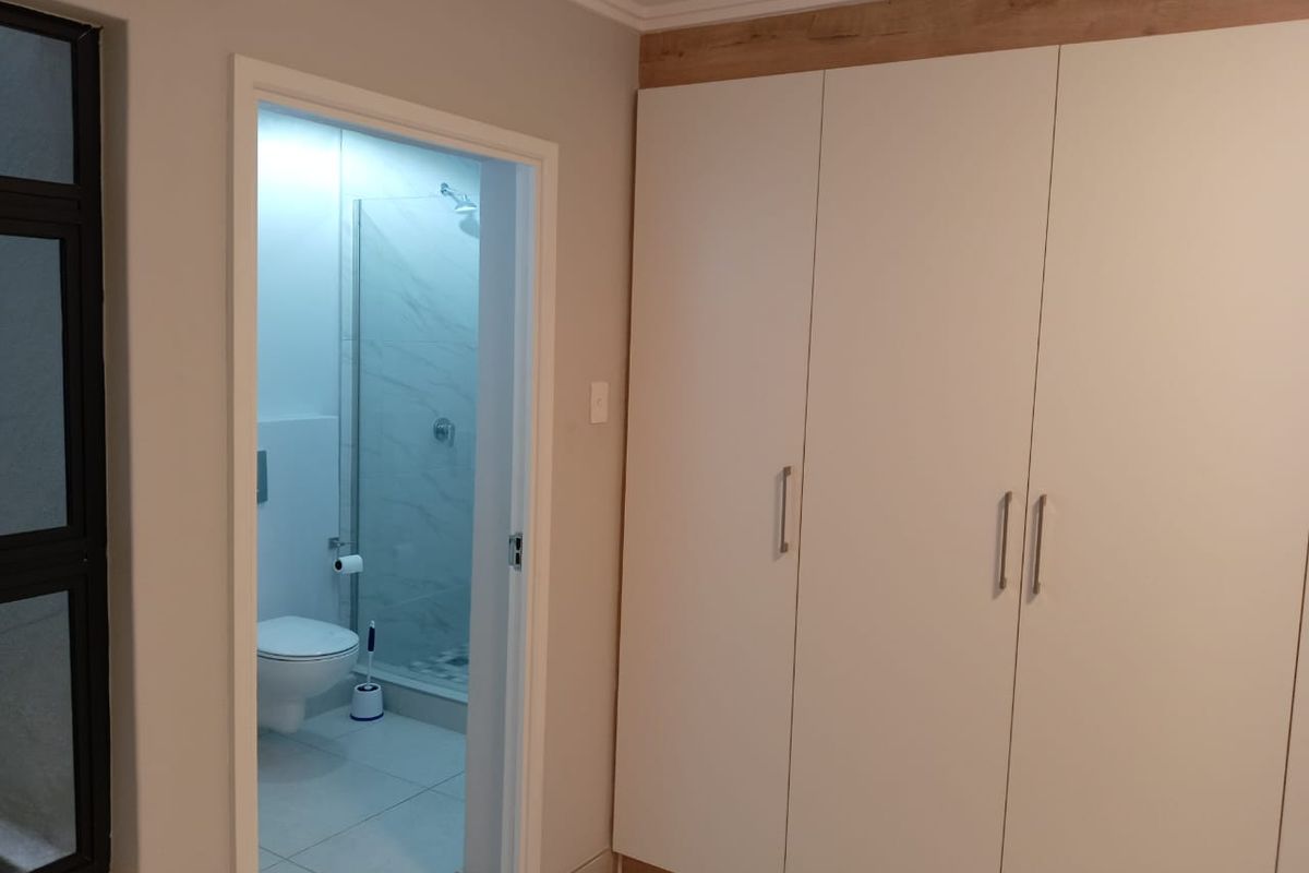 A bedroom featuring built-in floor-to-ceiling wardrobes with a modern finish, leading into an en-suite bathroom with a glass-enclosed shower.