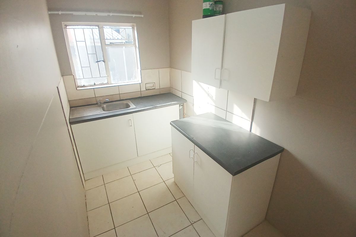 A compact kitchen featuring white cabinetry, dark laminate countertops, tiled flooring, and a single basin sink with a window for natural light.