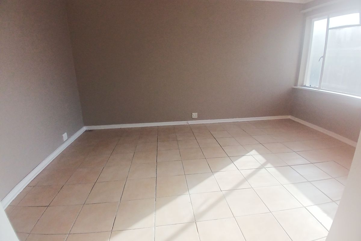 A bright, empty living room featuring neutral wall paint, tiled flooring, and a large window allowing for natural light.