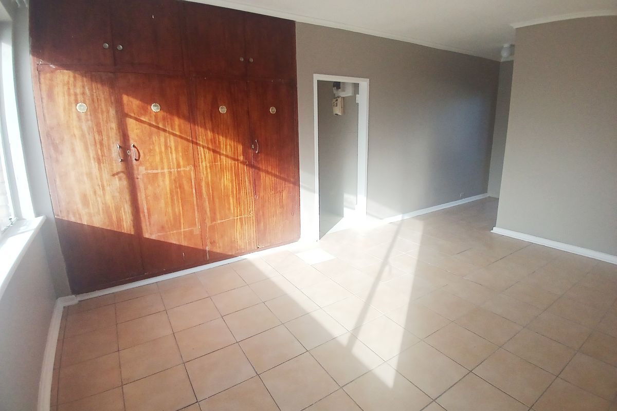 A spacious, empty bedroom featuring built-in wooden cupboards, tiled flooring, and neutral wall tones, offering a blank canvas for personalization.