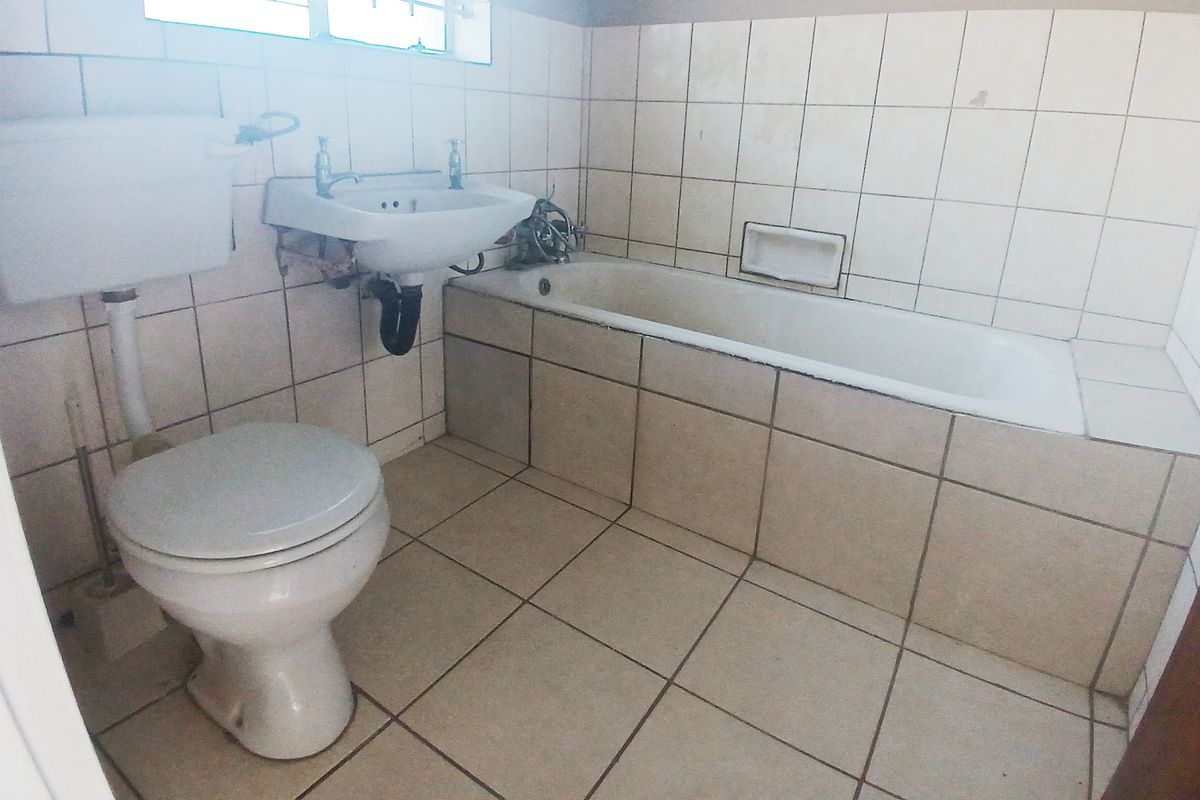 A dated bathroom featuring a standard bathtub, wall-mounted basin, and toilet with fully tiled walls and flooring.
