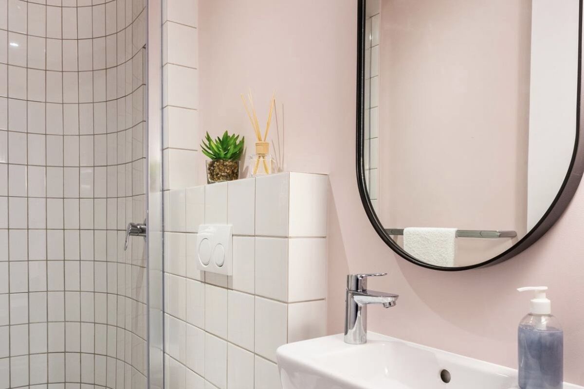 Modern bathroom featuring a wall-mounted toilet, a curved glass shower enclosure with white tiled walls, and a sleek wall-mounted basin with a black-framed mirror.