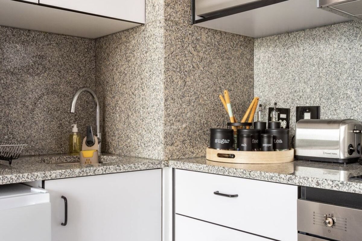 Compact kitchen featuring white cabinetry, granite countertops, a built-in oven, and a microwave, offering a functional and clean workspace.