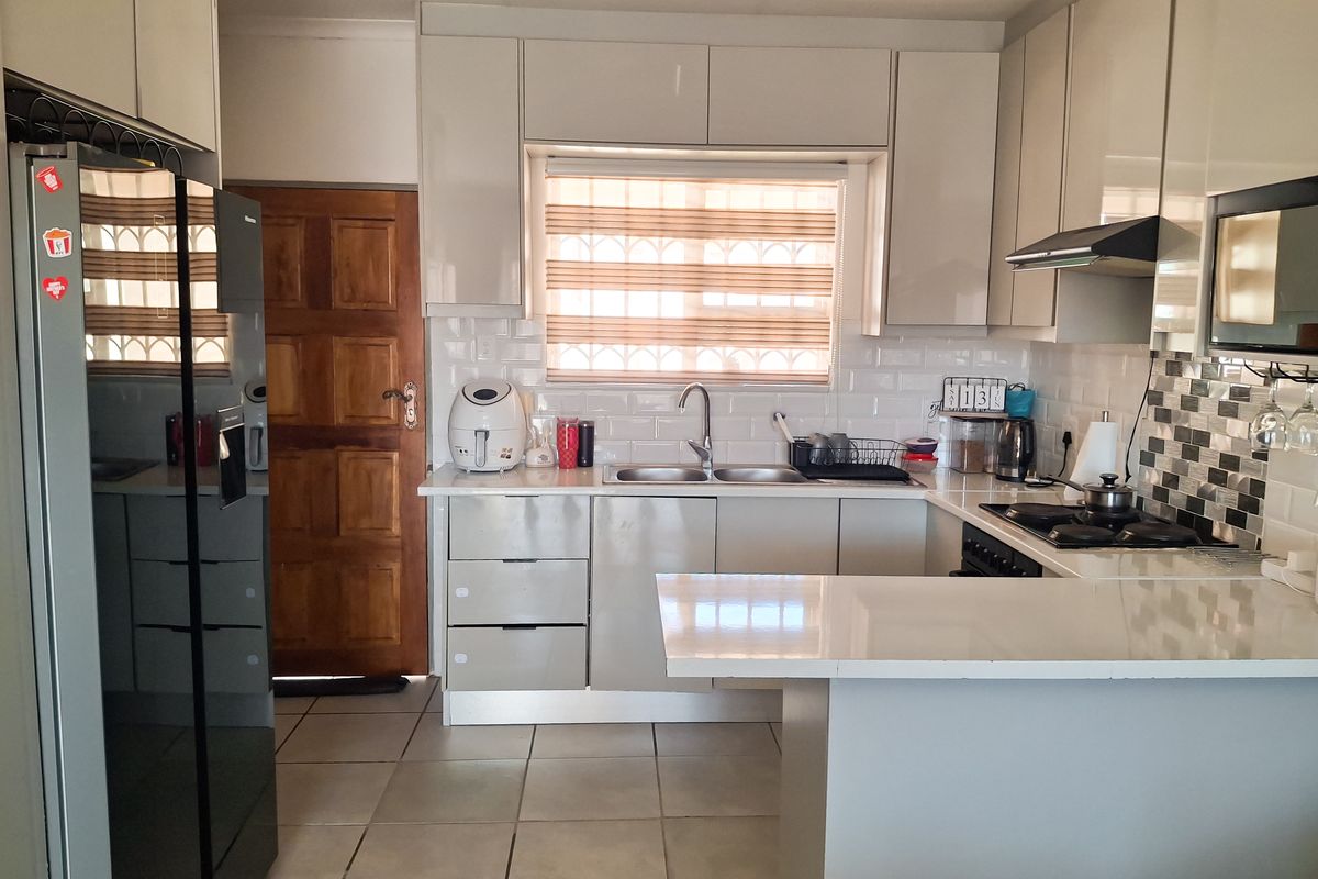 A functional kitchen featuring modern high-gloss cabinetry, subway tile backsplash, stone countertops, and integrated cooking appliances with tiled flooring.