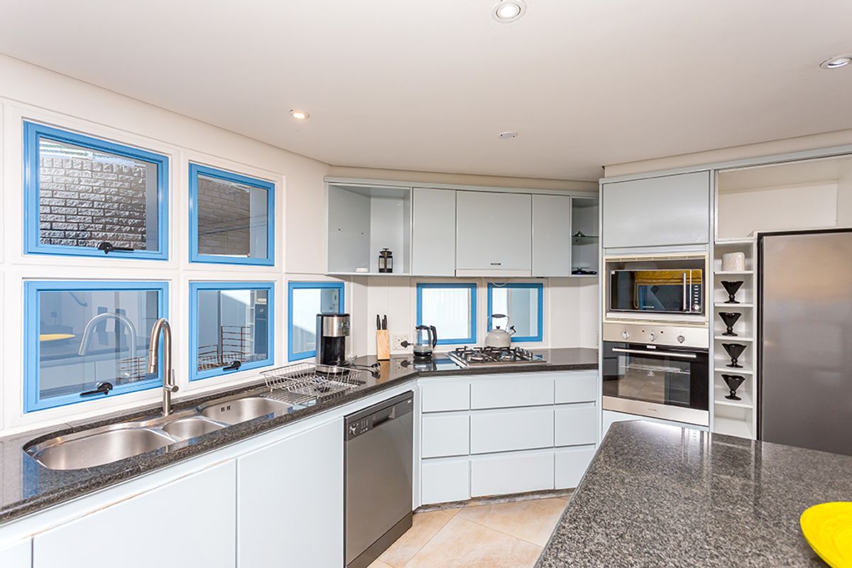 Modern kitchen featuring light blue cabinetry, granite countertops, integrated stainless steel oven, microwave, and gas hob with ample natural light from multiple windows.