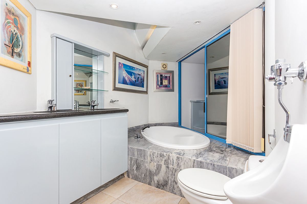 A functional bathroom featuring a built-in oval bathtub, vanity with dual basins, a toilet, and a wall-mounted urinal.