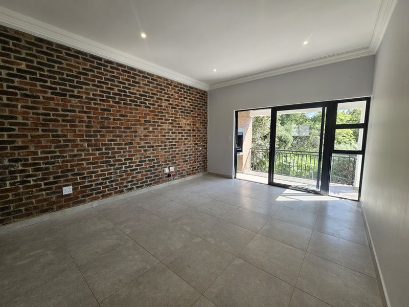 Spacious living area featuring a striking exposed brick feature wall, large sliding glass doors leading to a balcony, and modern neutral floor tiling.