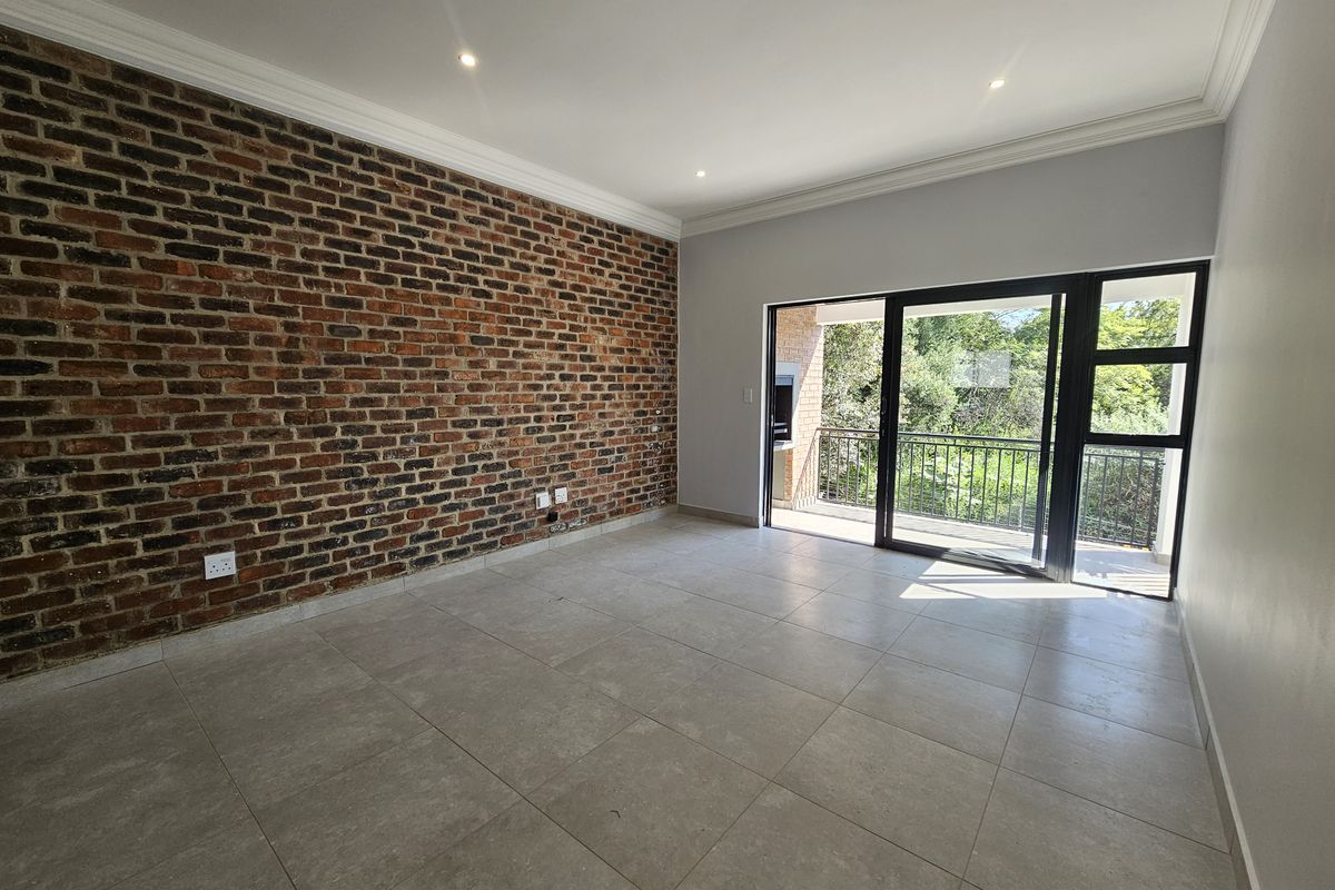 Spacious living area featuring a striking exposed brick feature wall, large sliding glass doors leading to a balcony, and modern neutral floor tiling.