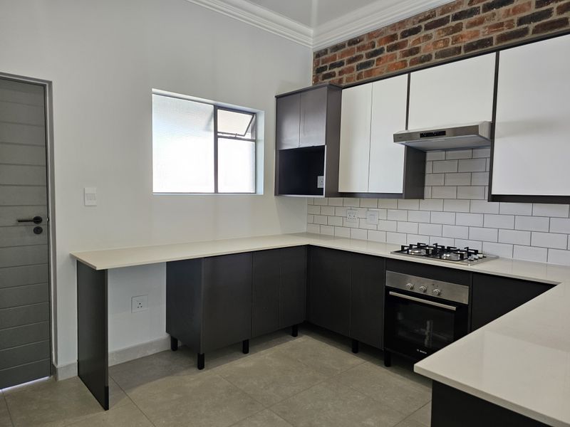 Modern kitchen featuring sleek dark cabinetry, white stone countertops, subway tile backsplash, exposed brick accent wall, and built-in oven with gas hob.