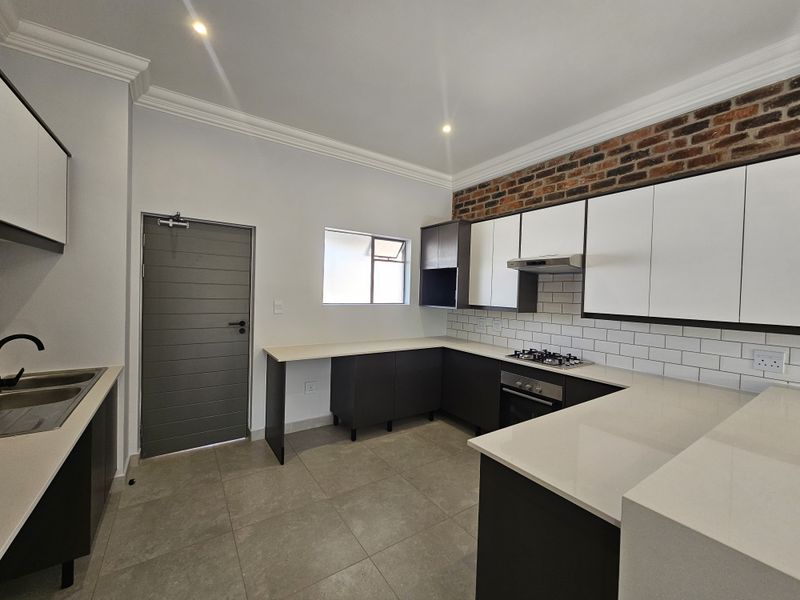 Modern kitchen featuring sleek cabinetry, stone countertops, a built-in gas hob, oven, extractor fan, and stylish exposed brick accent wall.