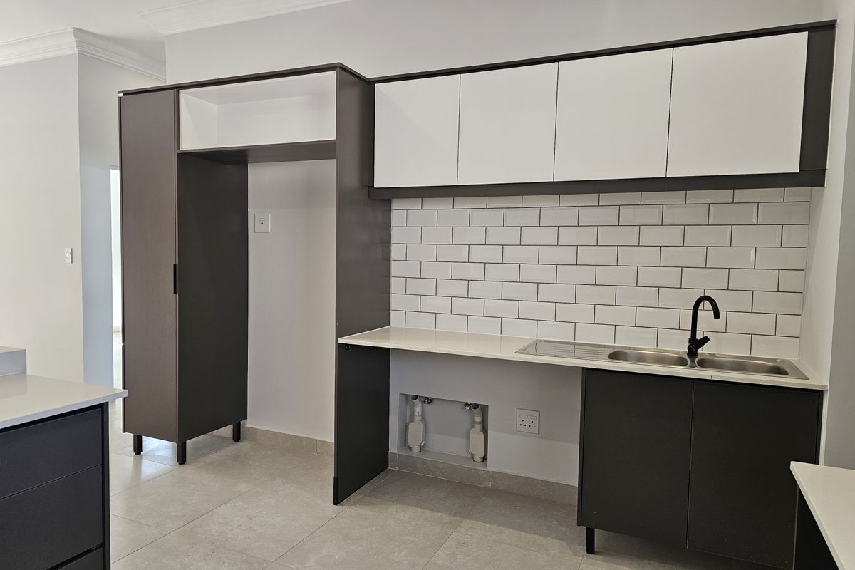 Modern kitchen area featuring two-tone cabinetry, subway tile backsplash, stone countertops, and a stainless steel double sink with a matte black faucet.