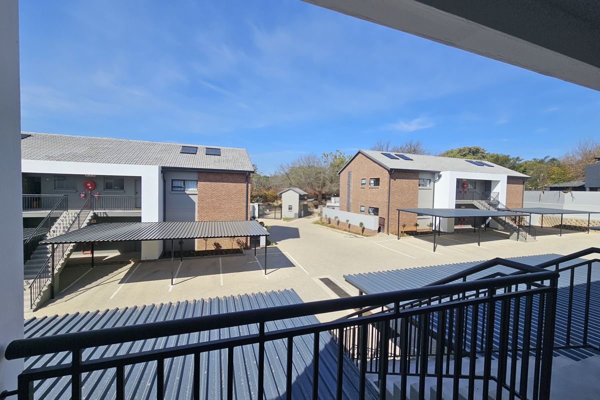 View of the apartment complex courtyard featuring paved parking areas, covered carports, and brick-faced residential buildings under a clear blue sky.