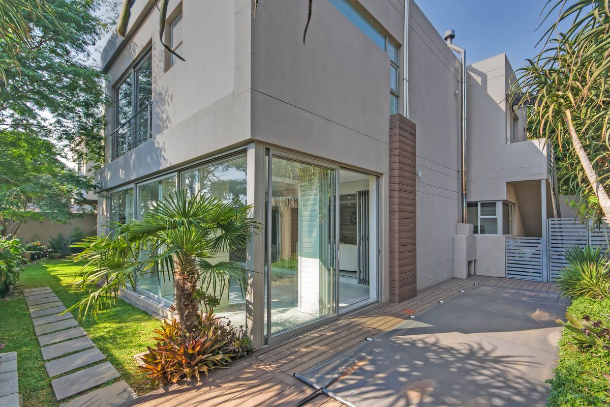 Modern rear elevation featuring extensive glass sliding doors, wooden decking, and a well-maintained garden with paved pathways.
