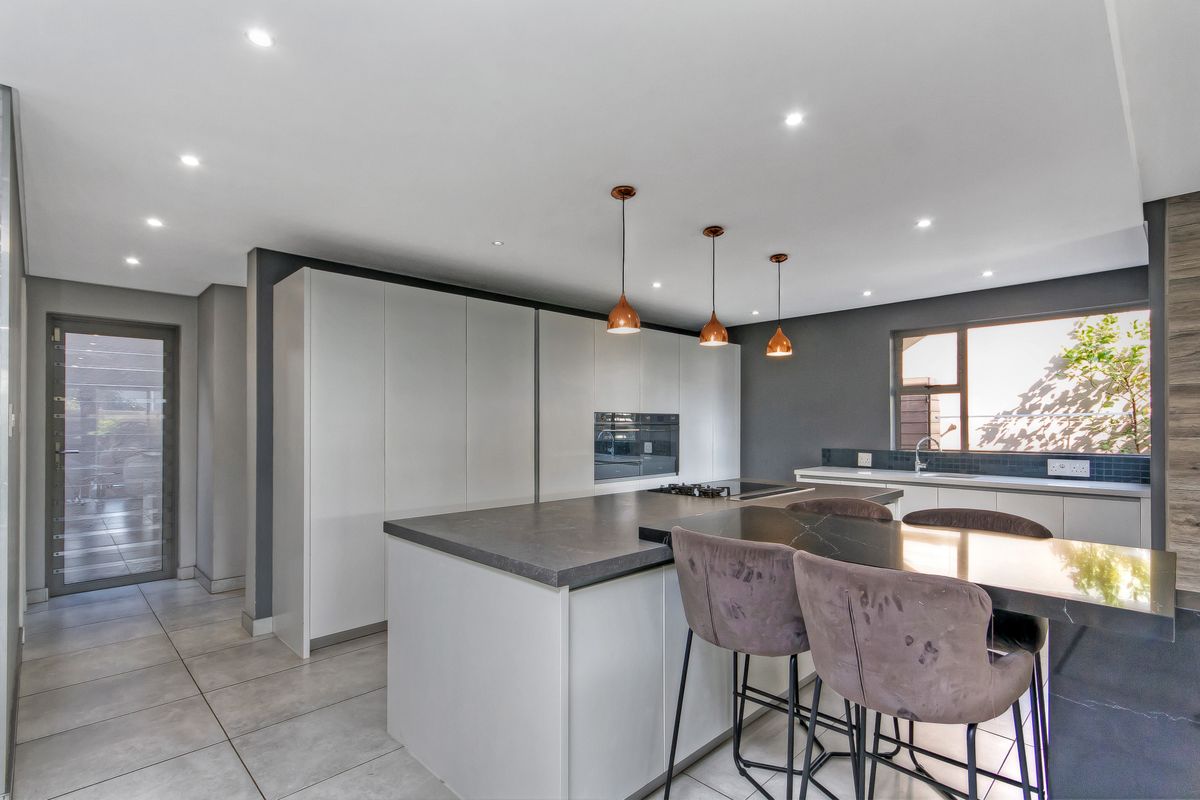 Modern kitchen featuring a large island with breakfast bar, sleek built-in cabinetry, integrated appliances, and contemporary pendant lighting.