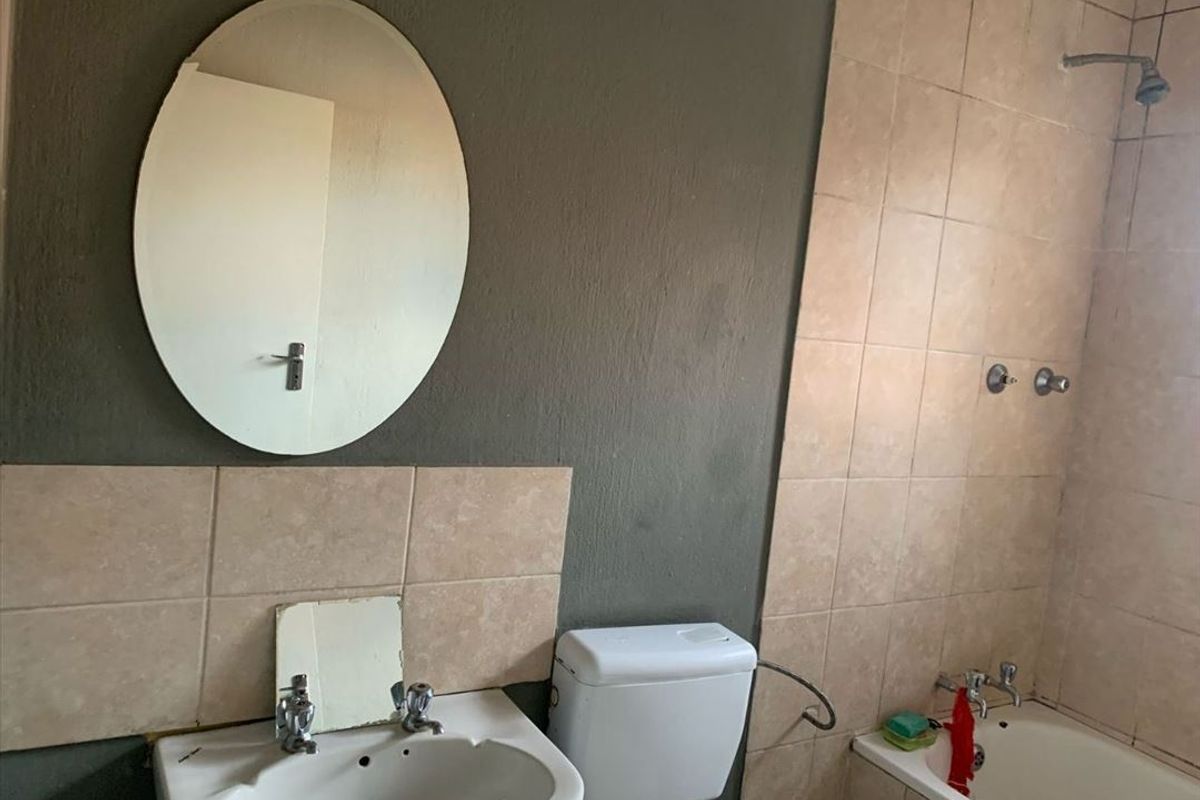 A functional bathroom featuring a bathtub with shower head, pedestal basin, and wall-mounted mirror, finished with neutral wall tiles and dark painted walls.