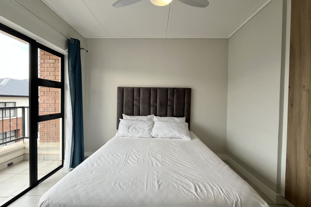 A well-maintained bedroom featuring built-in wooden cabinetry, a ceiling fan, and large glass sliding doors providing access to a private balcony.