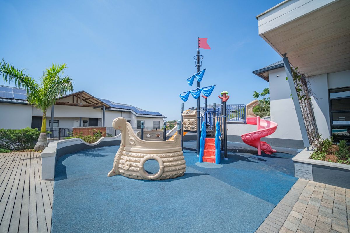 A well-maintained outdoor playground area featuring a ship-themed play structure, rubberized safety flooring, and paved walkways within a residential complex.