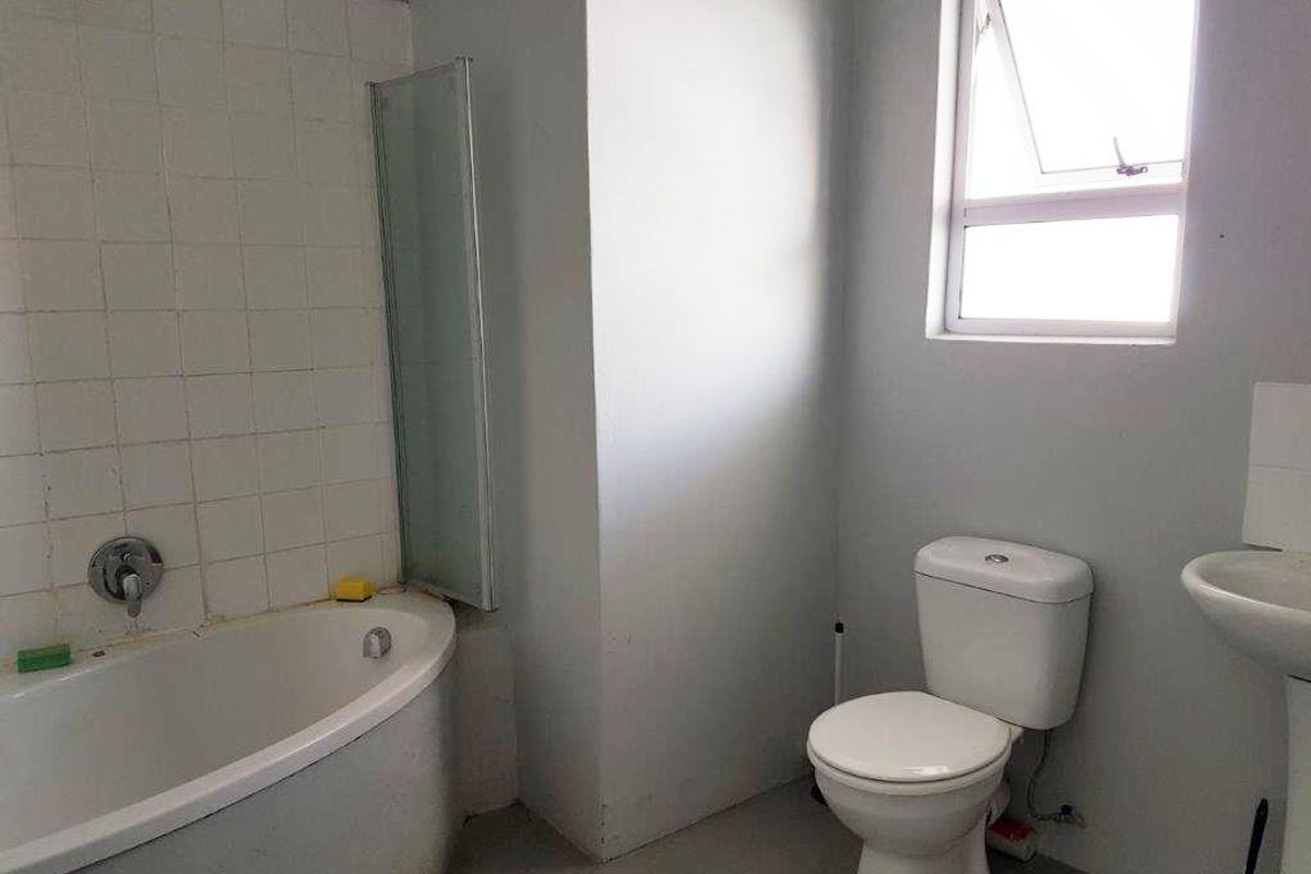 A functional bathroom featuring a bathtub with shower mixer, pedestal basin, and toilet, requiring cosmetic updates to improve its overall condition and aesthetic appeal.