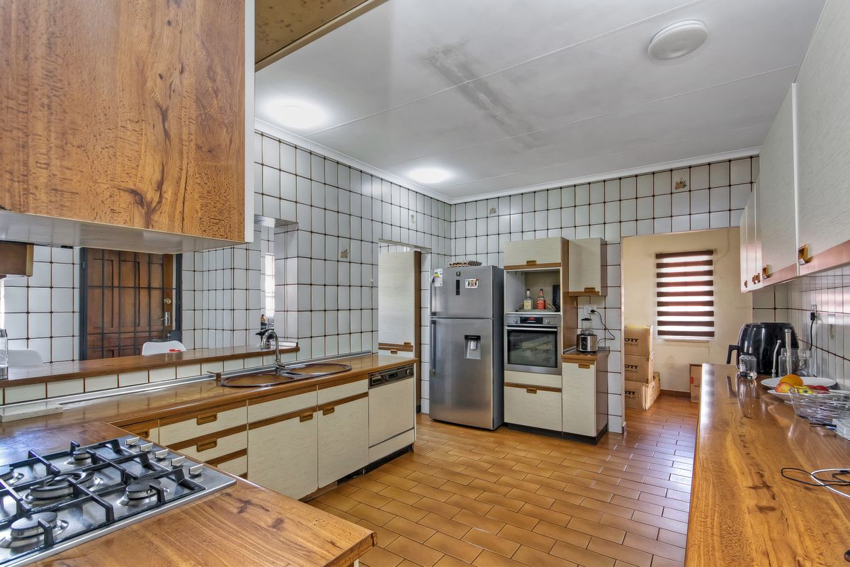 A functional kitchen featuring wooden countertops, built-in cabinetry, a gas hob, and a double sink, with tiled splashbacks and flooring throughout.