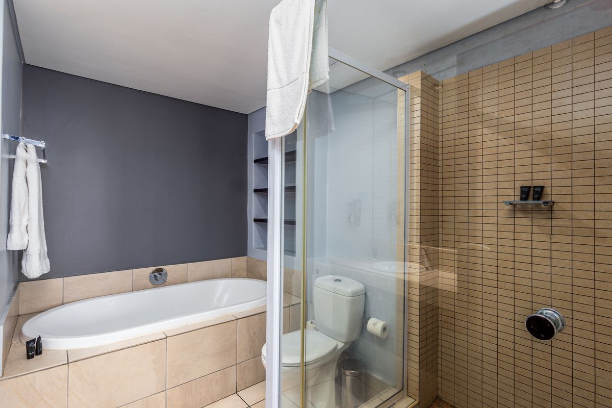 A functional bathroom featuring a built-in bathtub, a separate glass-enclosed shower, and a toilet with neutral-toned wall and floor tiling.