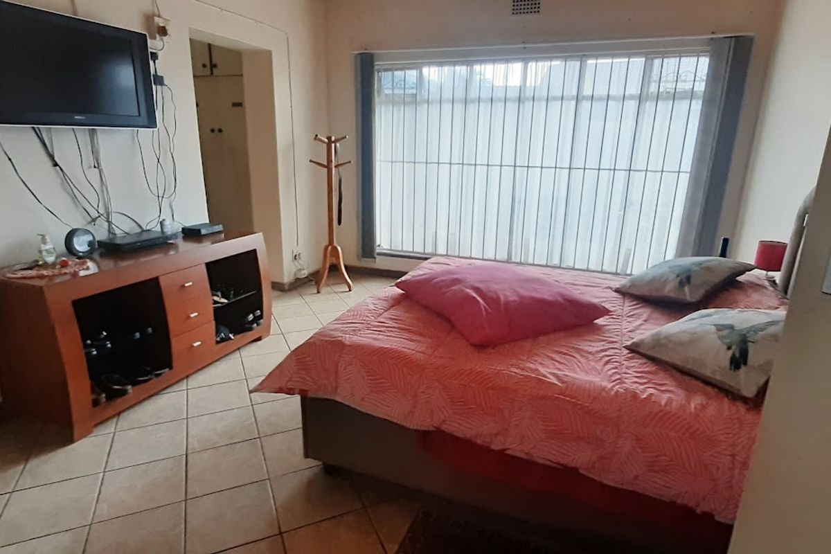 A functional bedroom featuring tiled flooring, a large window with vertical blinds, and built-in storage access.