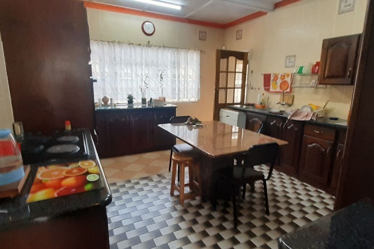 A dated kitchen featuring dark wood cabinetry, tiled flooring, and a central dining area, offering a functional layout with potential for modernization.