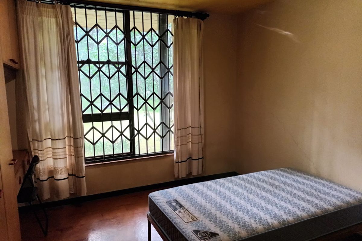A bedroom featuring a large window with security bars, wooden flooring, and built-in cabinetry.