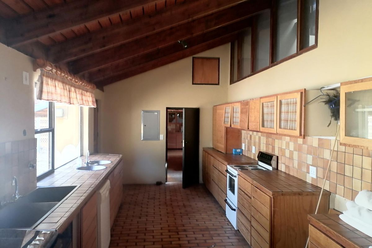 Spacious kitchen featuring exposed timber beam ceilings, tiled countertops, built-in wooden cabinetry, and a double sink, offering a rustic aesthetic.