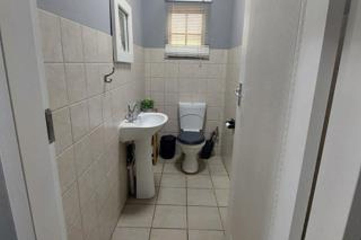 A compact guest bathroom featuring a pedestal sink, a standard toilet, and neutral wall tiling.
