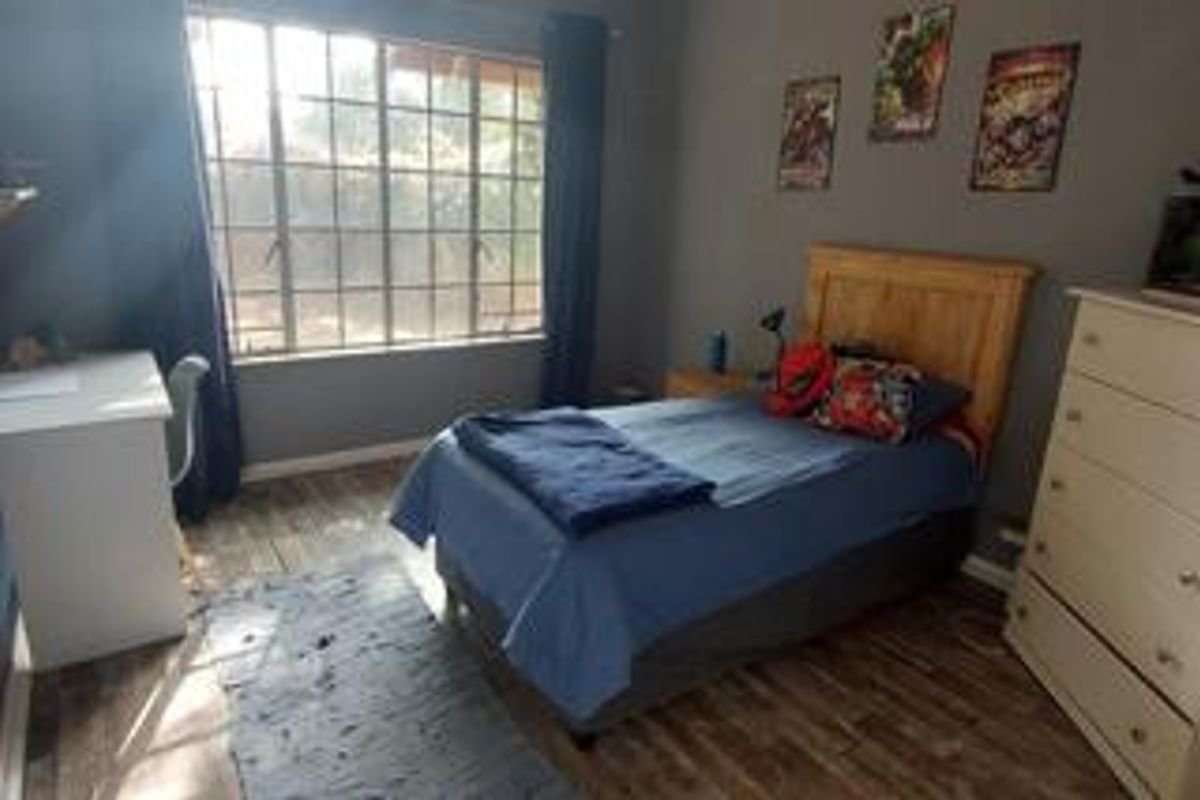 A functional bedroom featuring wood-look flooring, a large window with security bars, and neutral wall finishes.