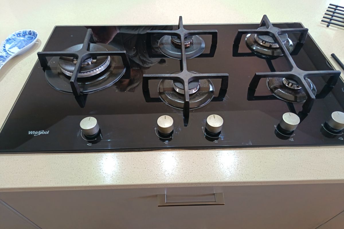 A modern black glass Whirlpool gas cooktop integrated into a light-colored stone countertop with built-in cabinetry below.