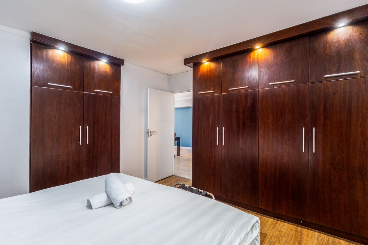 A well-maintained bedroom featuring extensive dark wood built-in cabinetry with integrated downlighting and warm-toned laminate flooring.