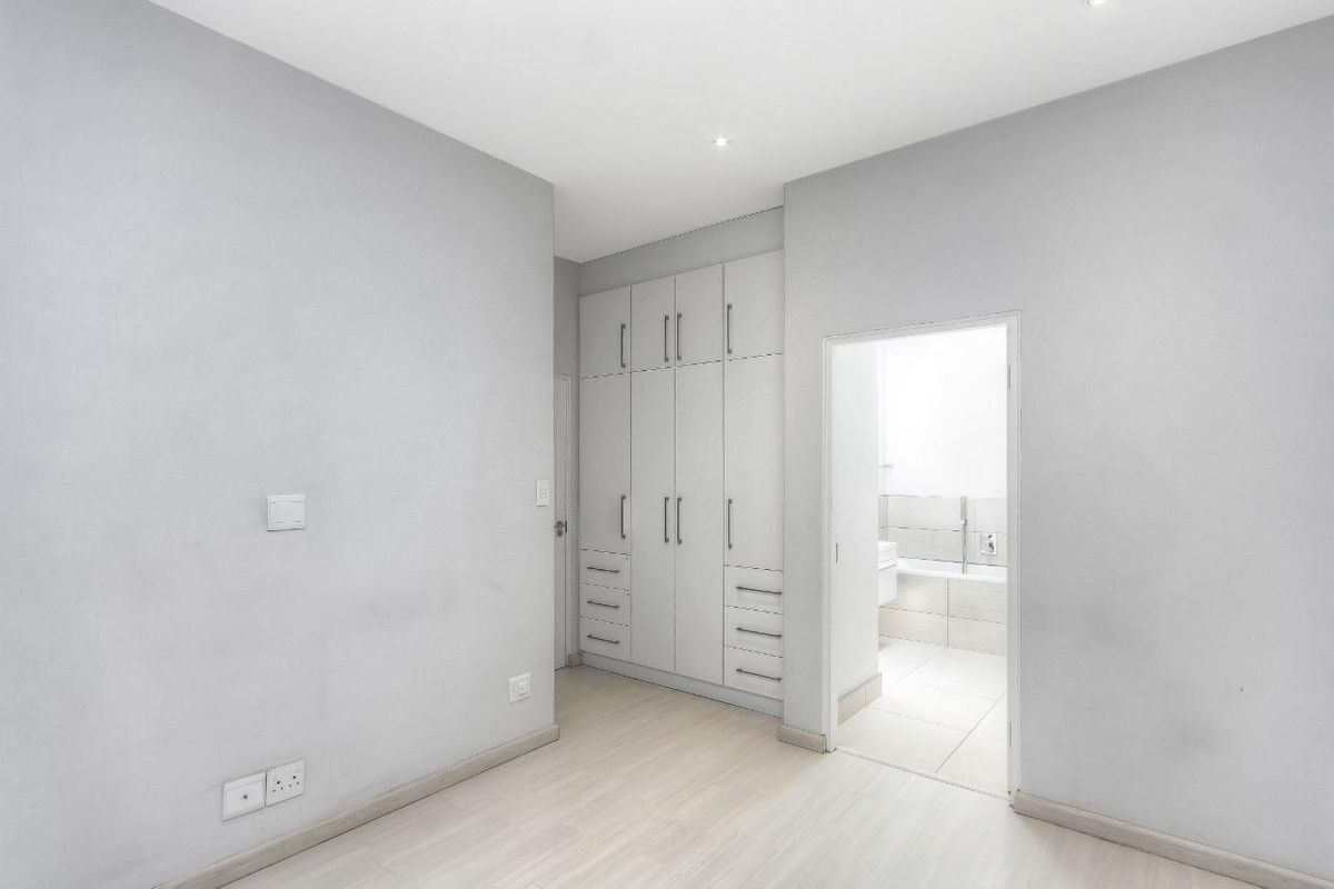 A bright bedroom featuring built-in floor-to-ceiling cabinetry and direct access to an en-suite bathroom with neutral finishes.