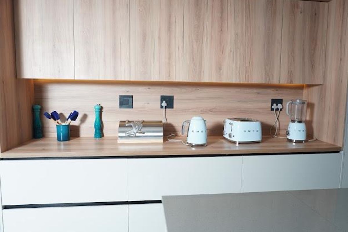 Modern kitchen featuring light wood-grain cabinetry, white handleless drawers, and integrated under-cabinet lighting with a clean, contemporary aesthetic.
