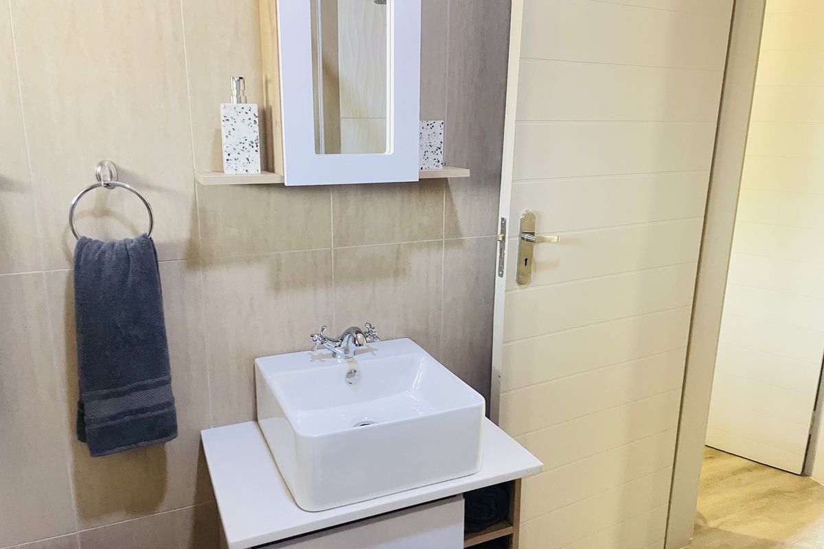 A modern bathroom featuring a square vessel sink, vanity cabinet, wall-mounted mirror cabinet, and neutral wall tiling.