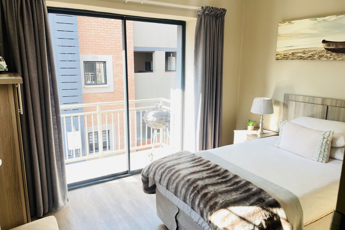 A well-maintained bedroom featuring laminate flooring, neutral walls, and sliding glass doors that open onto a private balcony.