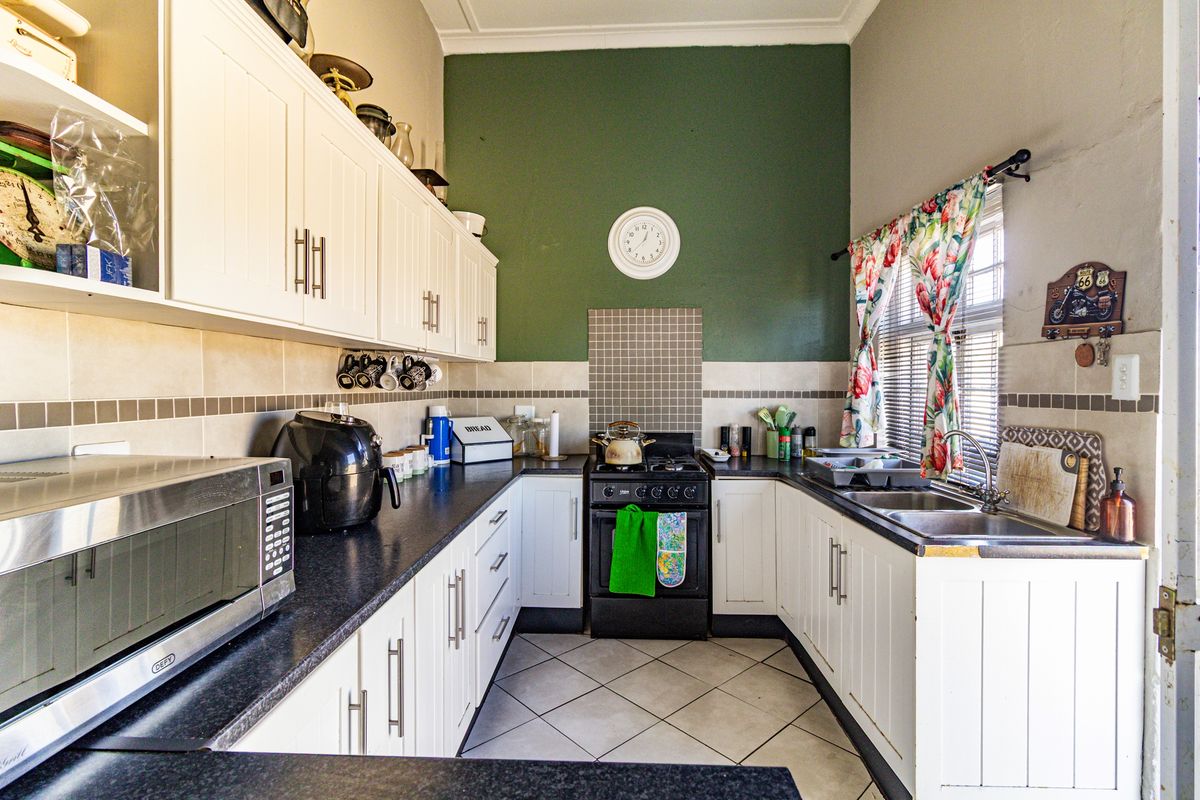 A functional kitchen featuring white cabinetry, dark countertops, a built-in stove with extractor, and a double-basin sink with tiled splashbacks.