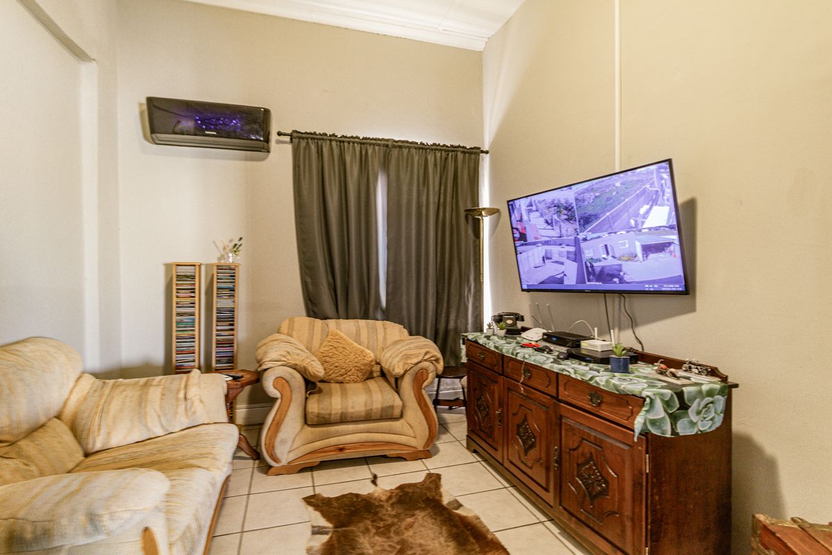 A living room featuring tiled flooring, high ceilings with crown molding, and a wall-mounted air conditioning unit.
