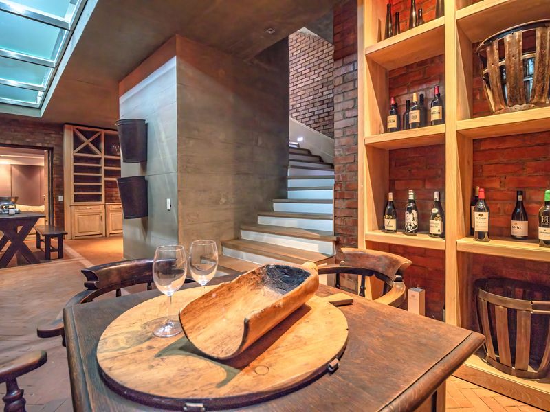 A sophisticated interior space featuring exposed brickwork, built-in timber wine shelving, a staircase, and a skylight, creating a warm and character-filled atmosphere.